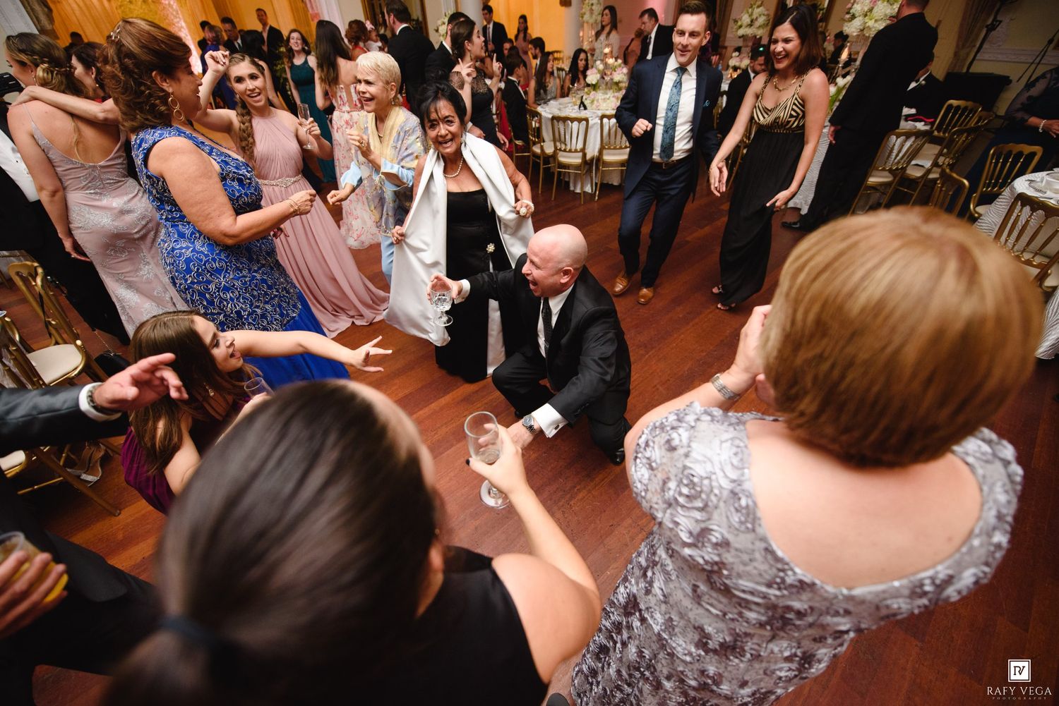 Guests dancing and celebrating at an elegant wedding reception on a wooden dance floor.