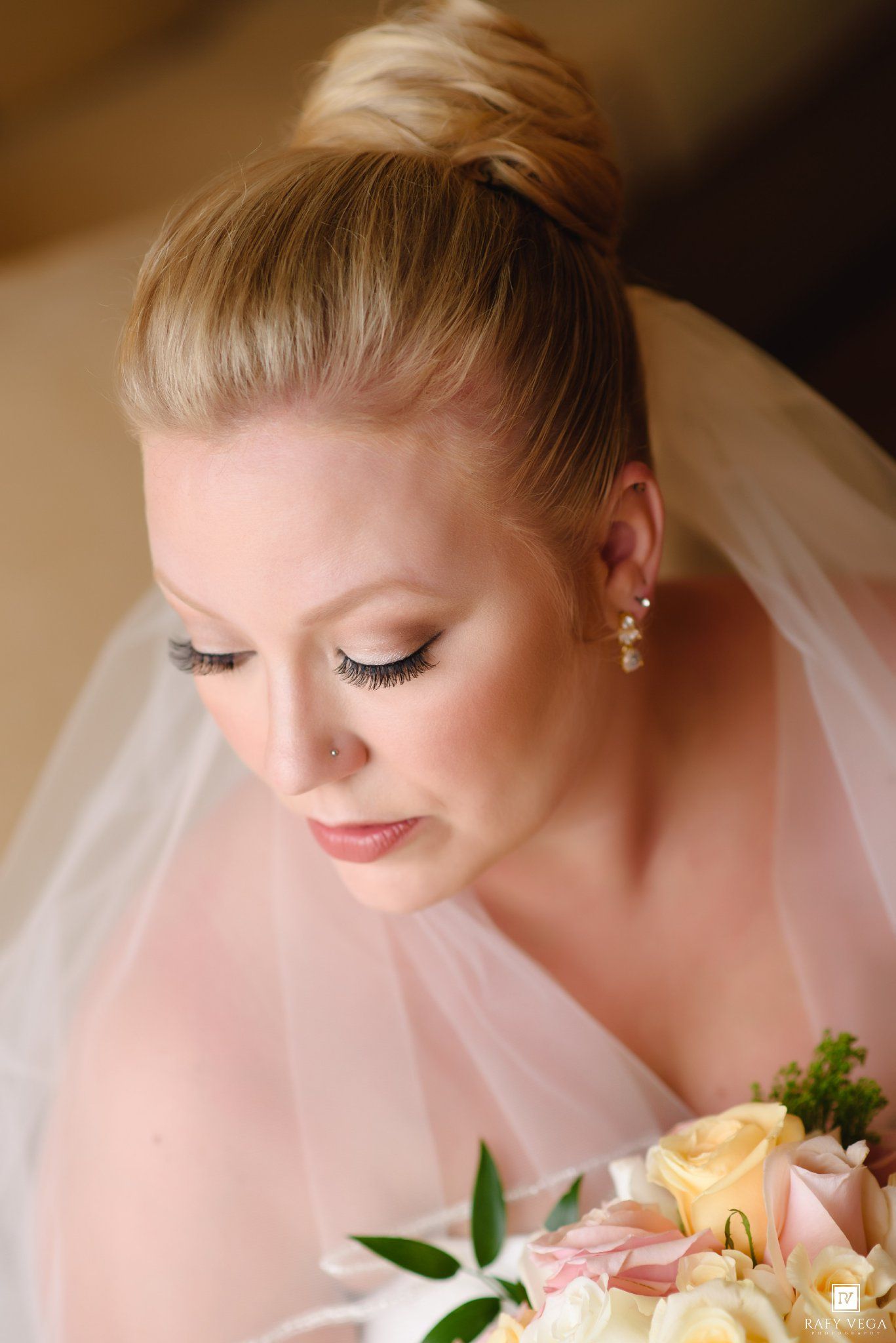 Elegant bride with blonde updo and veil holding a pastel rose bouquet on her wedding day.