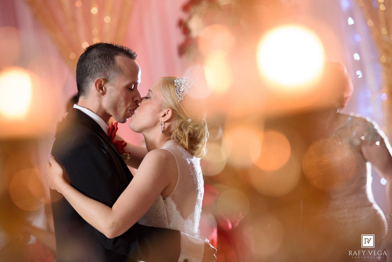 A bride and groom share a romantic kiss during their wedding reception, surrounded by warm bokeh lights.