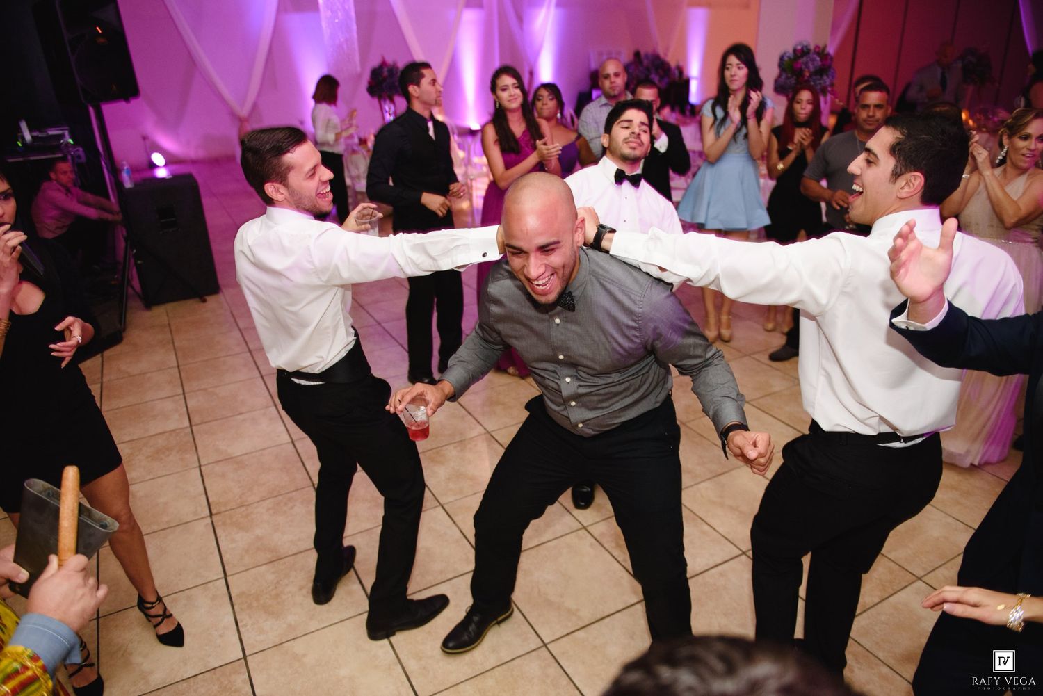 Men dancing energetically on a wedding reception dance floor with guests celebrating in the background.