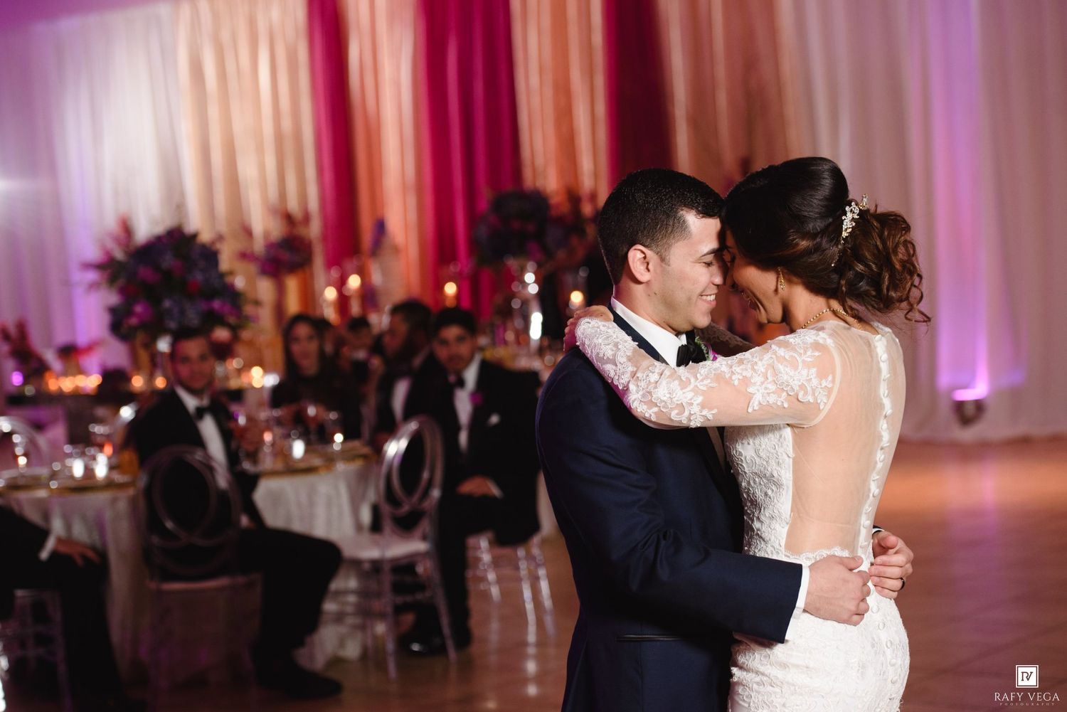 Bride and groom share their first dance at an elegant wedding reception with pink and white draping.