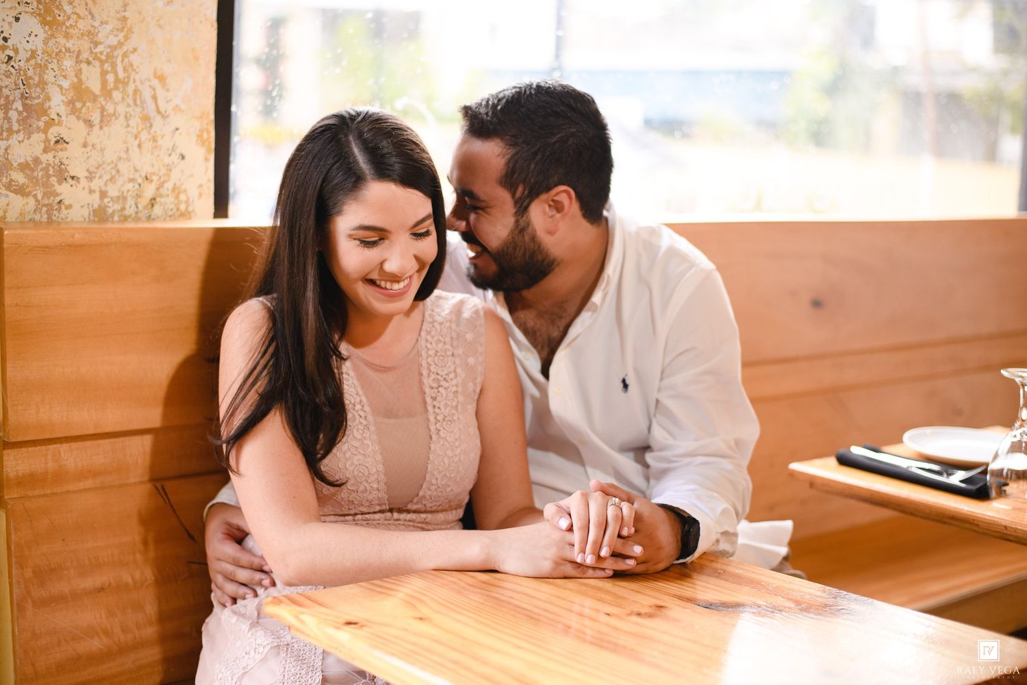 Couple sharing a romantic moment at a wooden restaurant booth, smiling and holding hands.