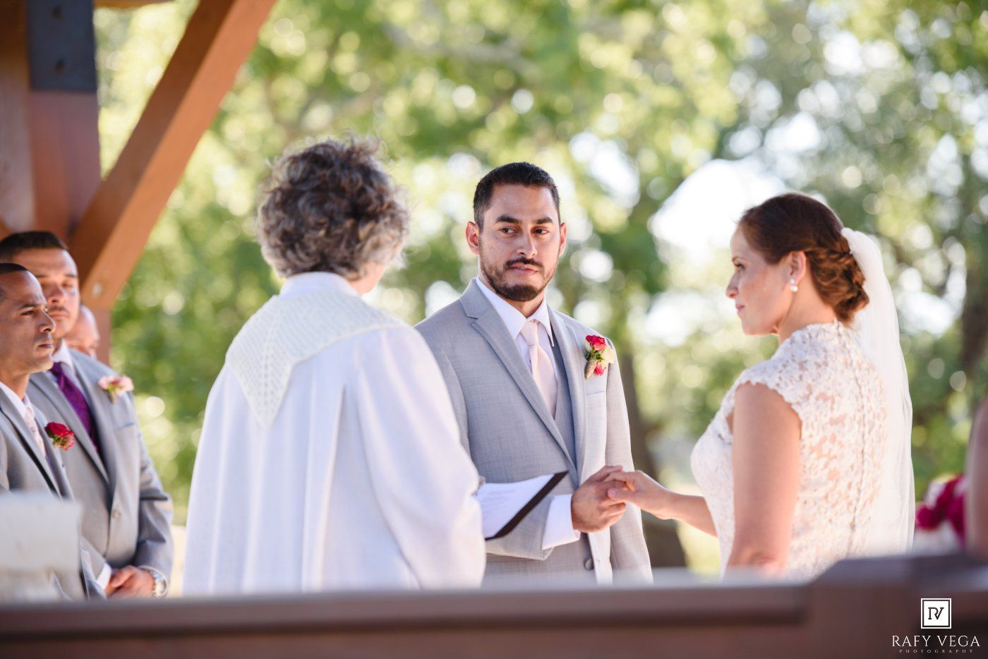 Groom exchanges rings with bride during outdoor wedding ceremony with officiant and groomsmen.