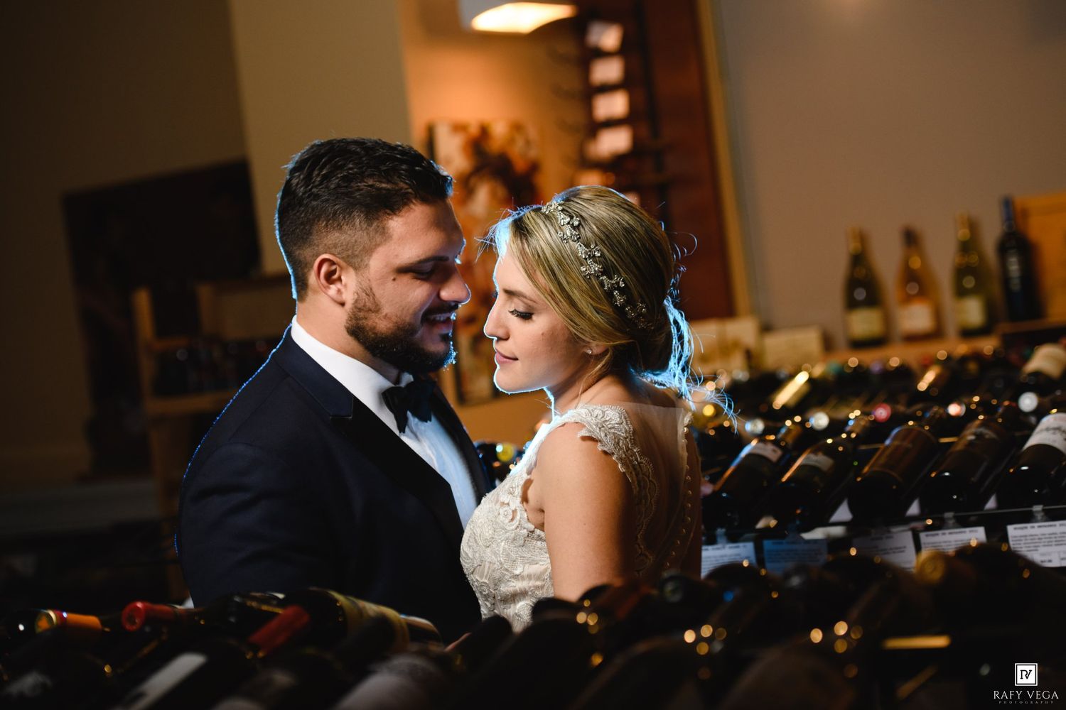 Newlywed couple share romantic moment surrounded by wine bottle displays in stunning wedding portrait.