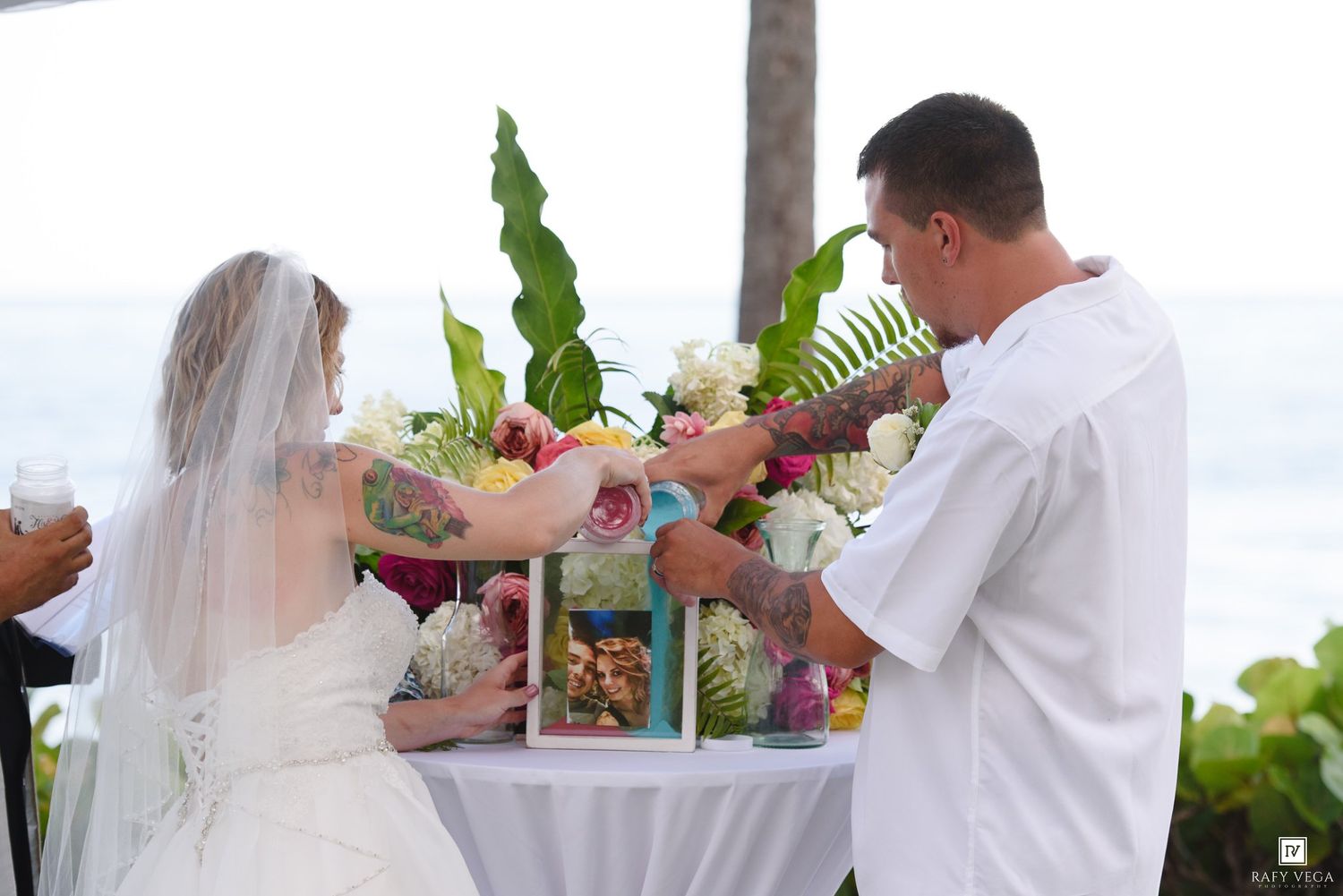 Bride and groom exchanging rings at outdoor beach wedding ceremony with tropical floral arrangement.