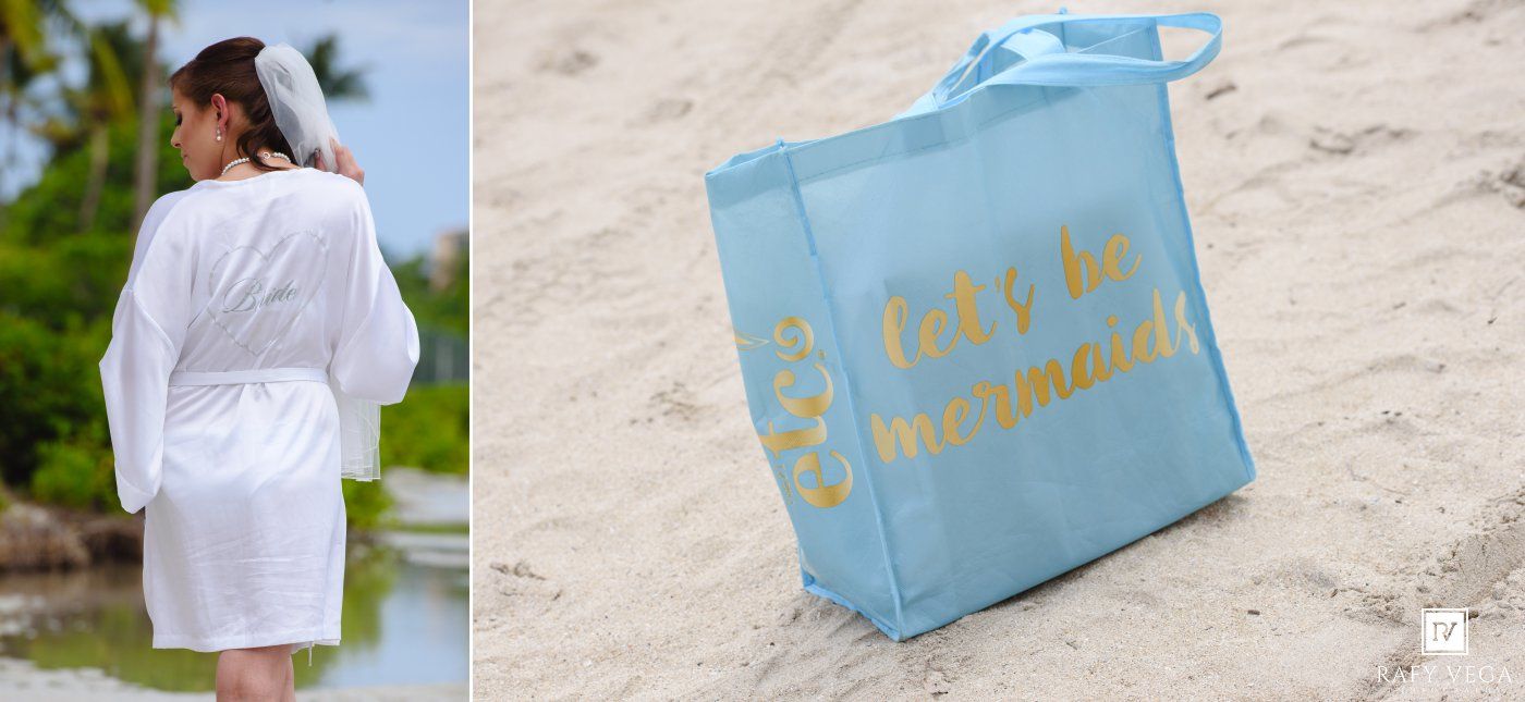 Bride in white robe on beach beside a light blue tote bag with gold text reading lets be mermaids on sand.