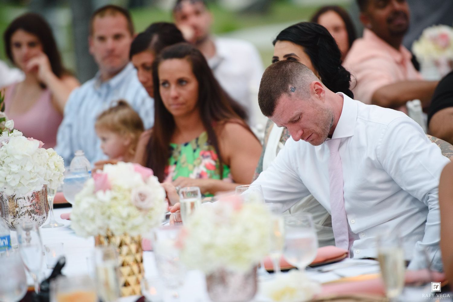 Wedding guests seated at an elegantly decorated outdoor reception table with floral centerpieces.