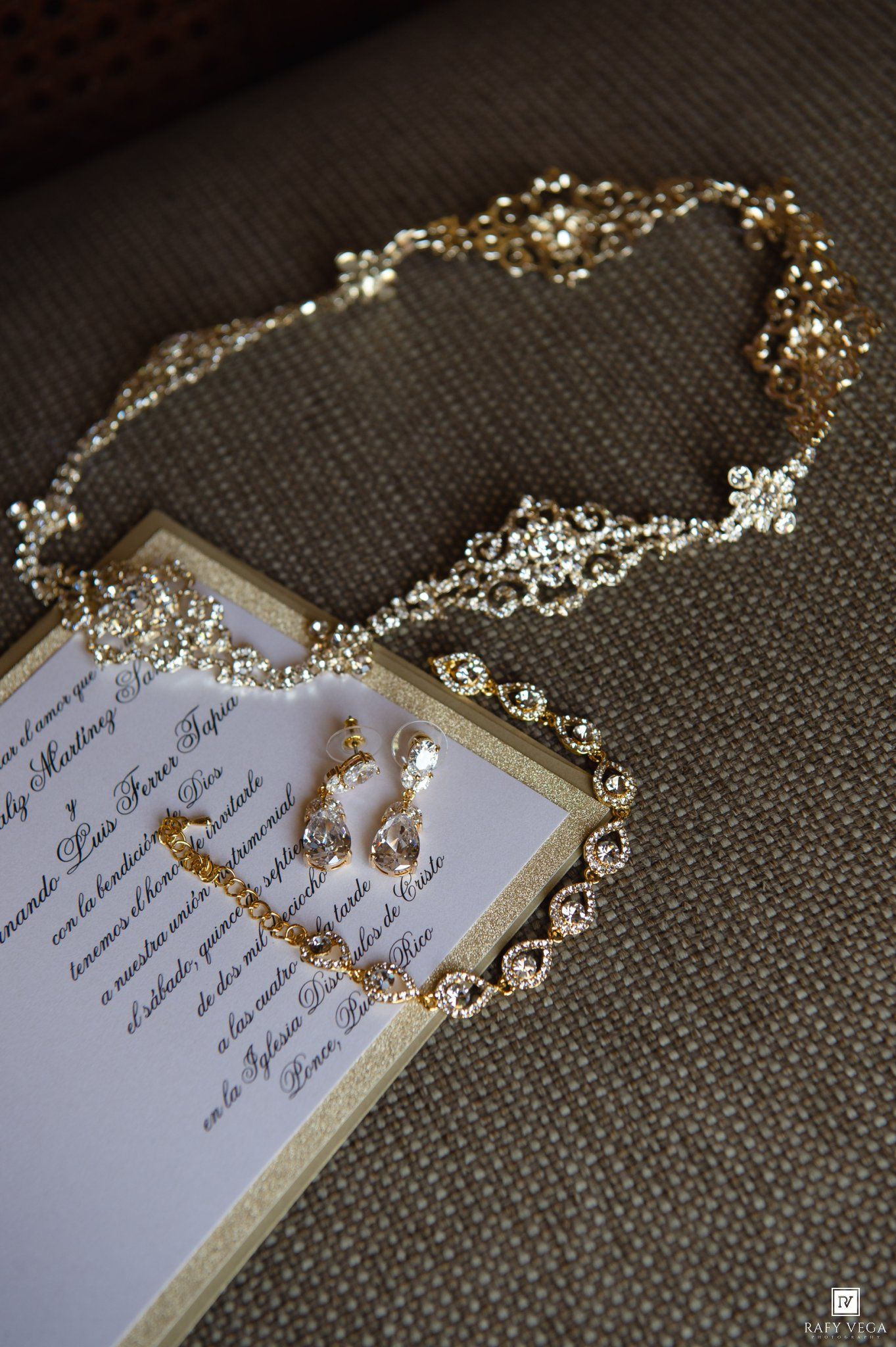 Gold rhinestone necklace and crystal drop earrings displayed beside an elegant wedding invitation on a textured burlap surface.