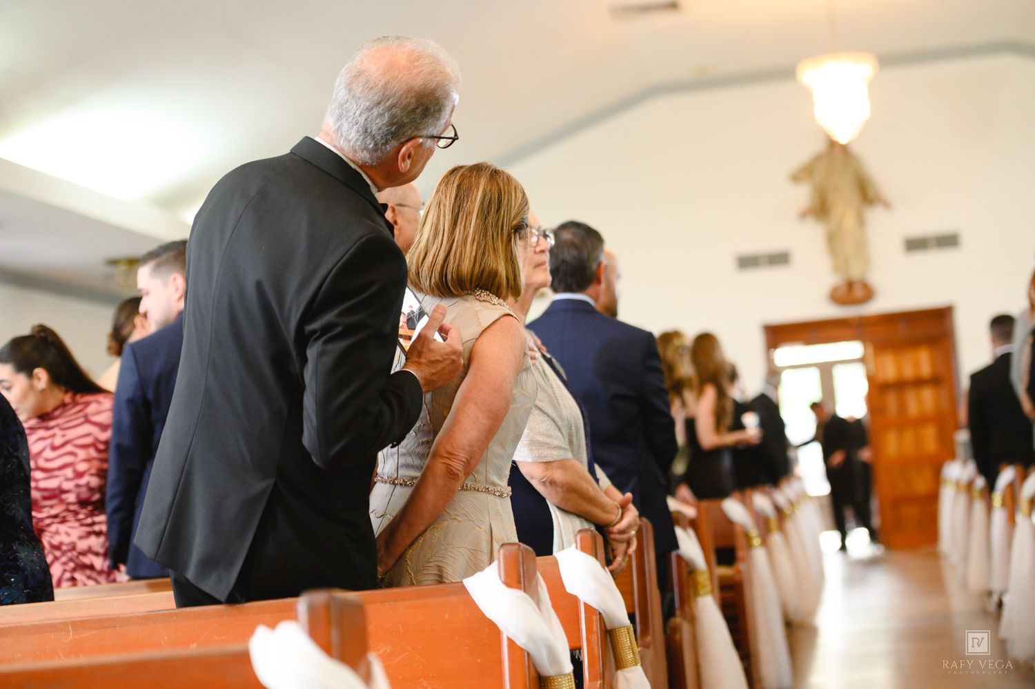 Couple sharing an intimate moment in a church pew during a wedding ceremony with guests seated nearby.