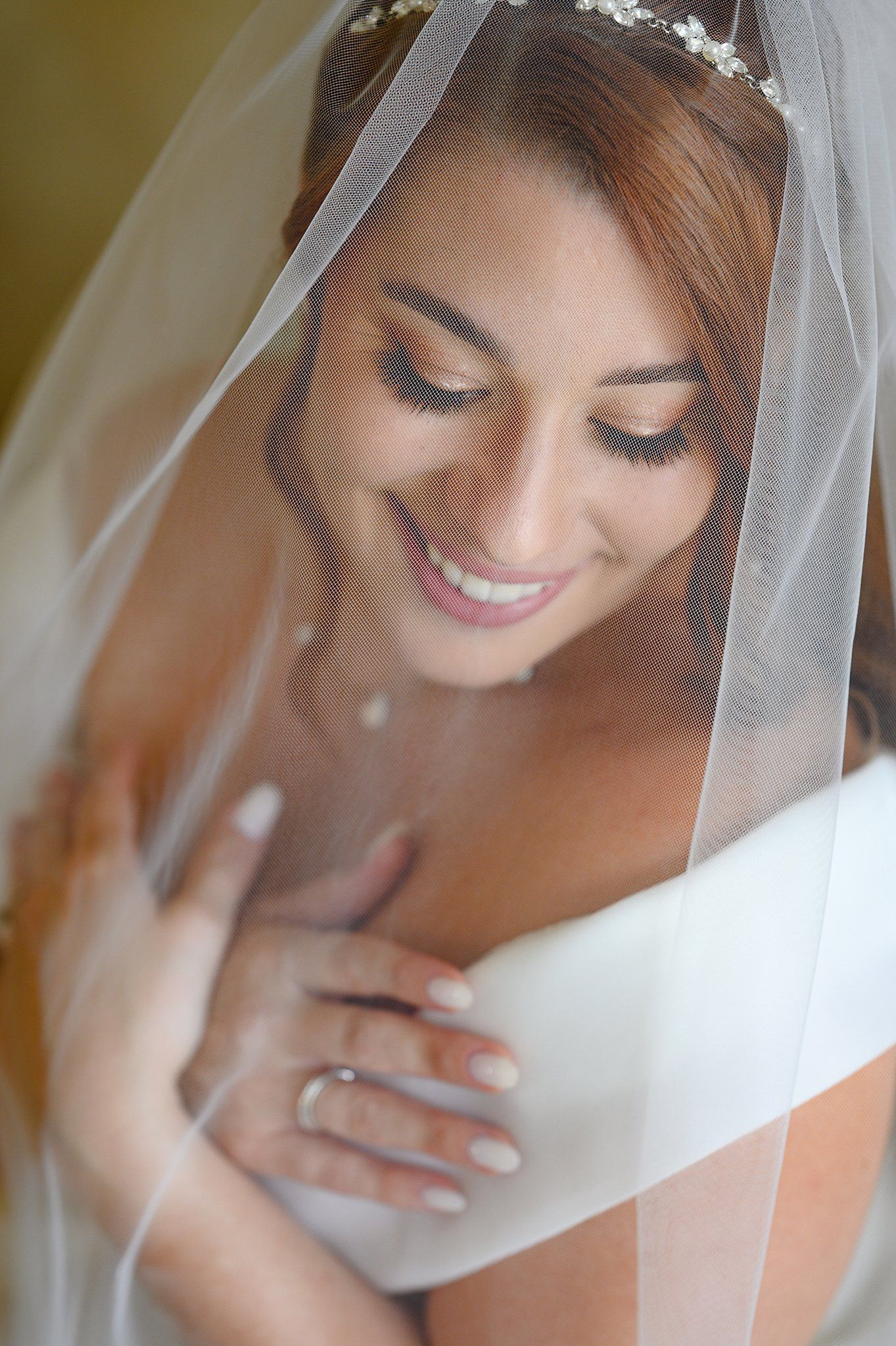Smiling bride draped in sheer veil wearing floral tiara and engagement ring on her wedding day.