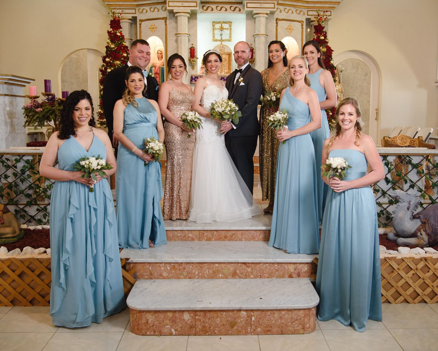 Wedding party posing in church with bride, groom, and bridesmaids in blue gowns holding bouquets.