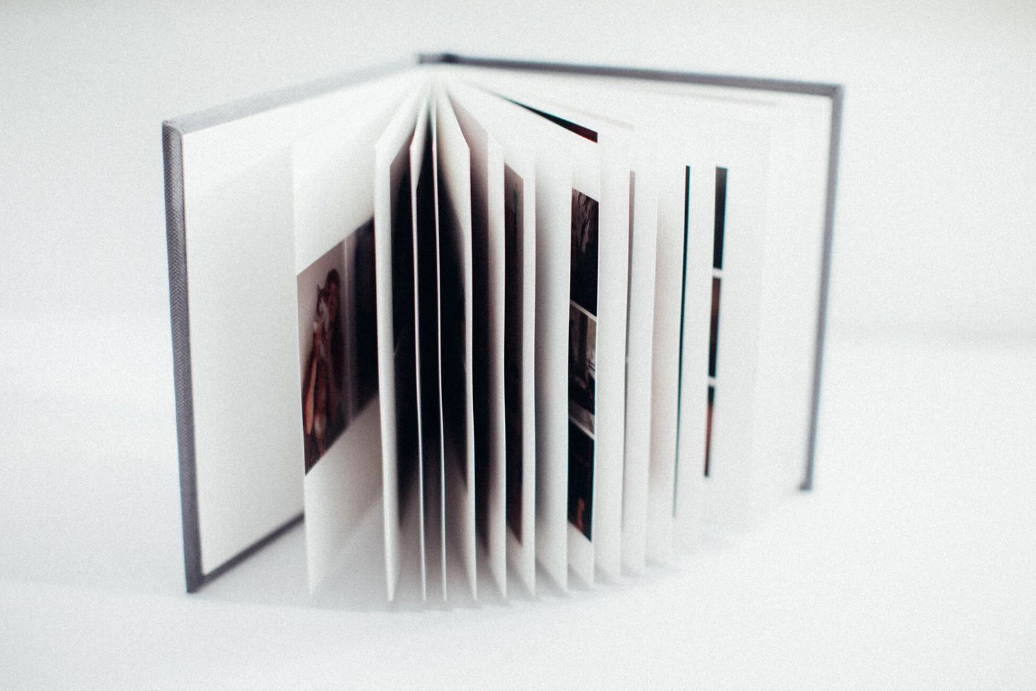 Open hardcover photo book with multiple pages fanned out, displayed on a white background.