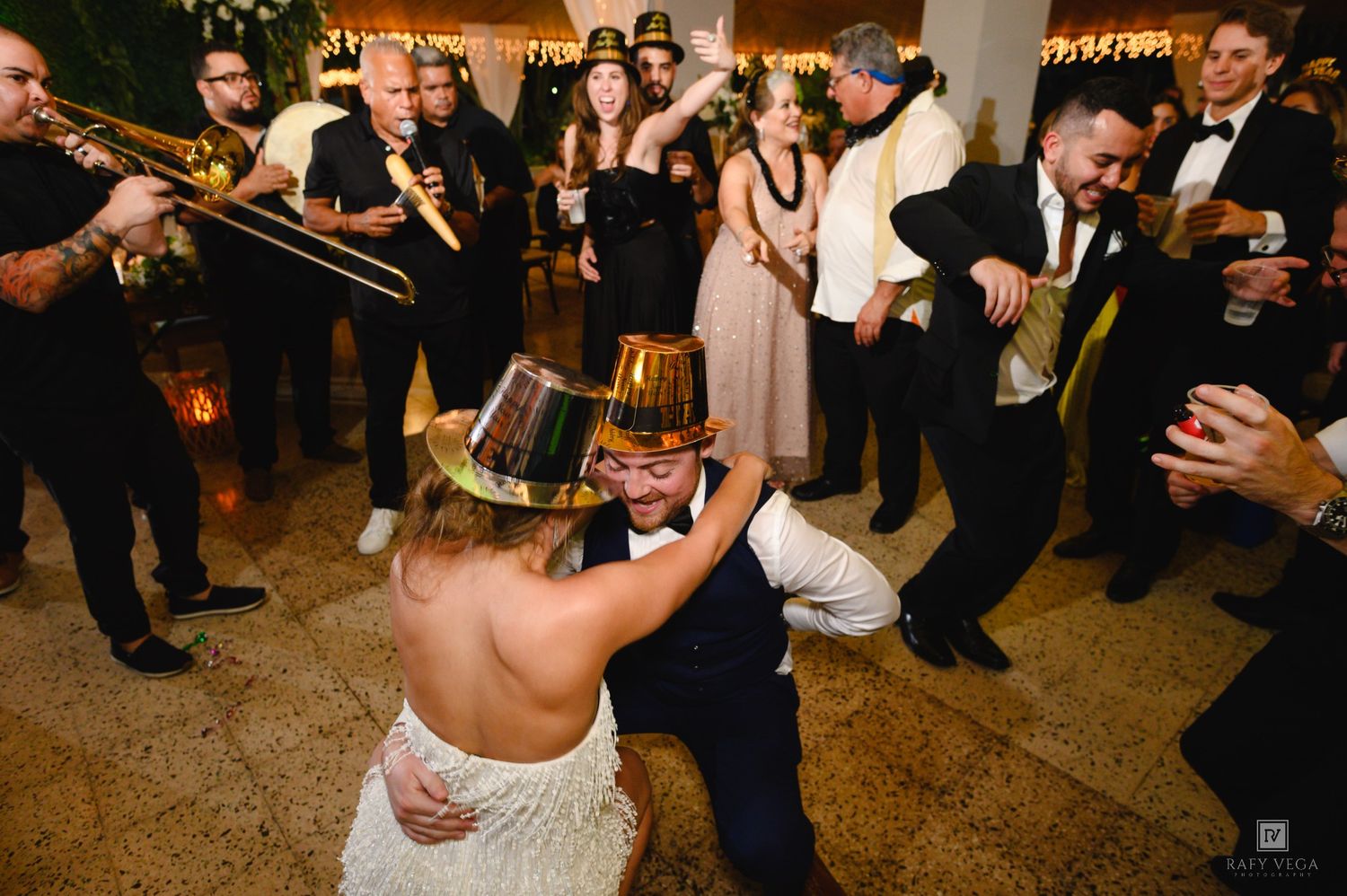 Bride and groom dancing joyfully at wedding reception with live brass band performing in background.