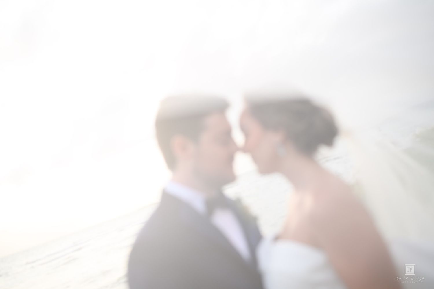 Dreamy blurred wedding couple almost kissing in soft white light, bride in veil and groom in tuxedo.