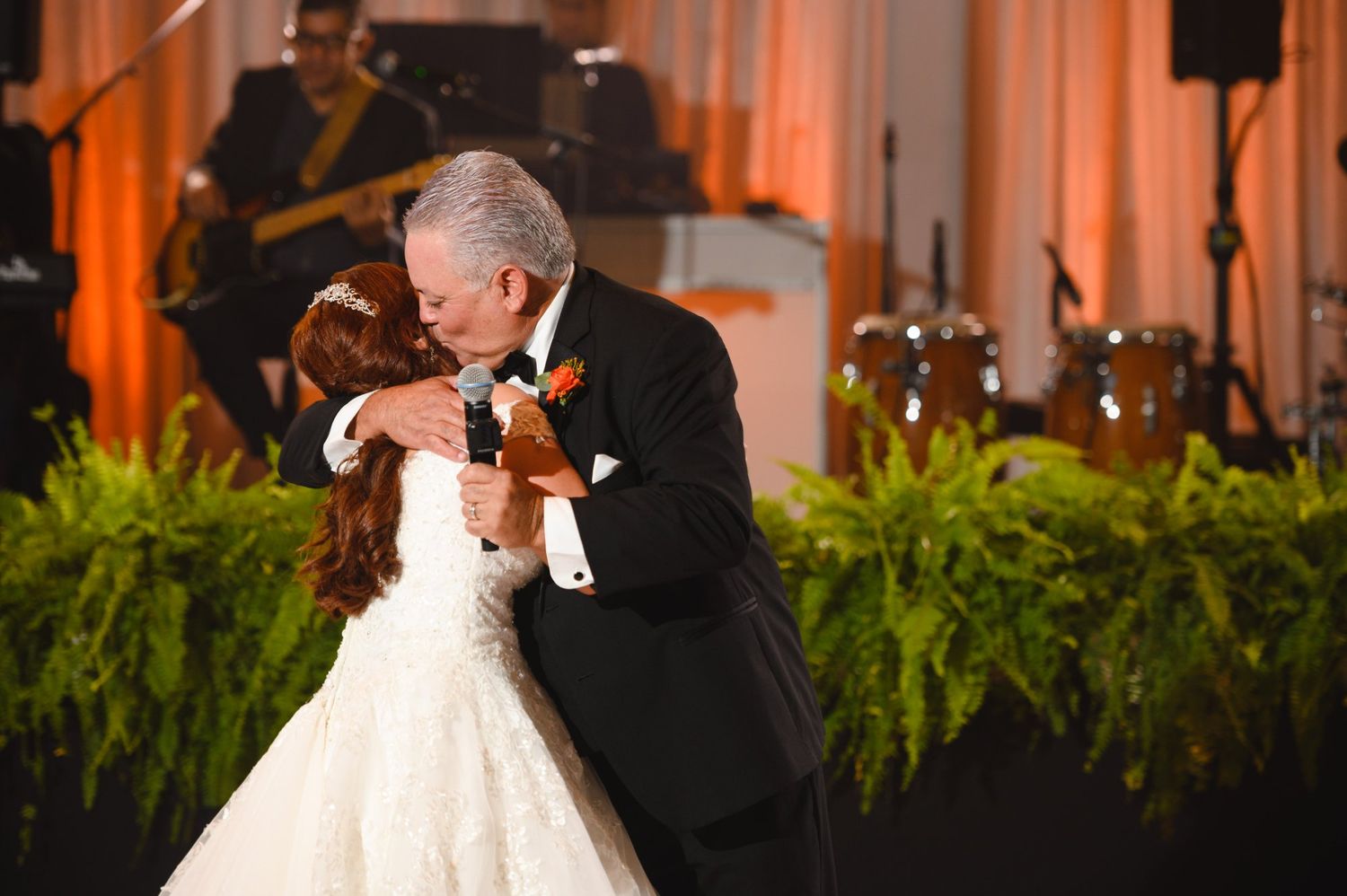 Father and bride share emotional first dance embrace at elegant wedding reception with live band.