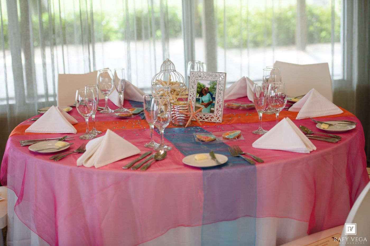 Elegant round banquet table with pink ombre tablecloth, white napkins, silver cutlery, and crystal glassware for a formal event.
