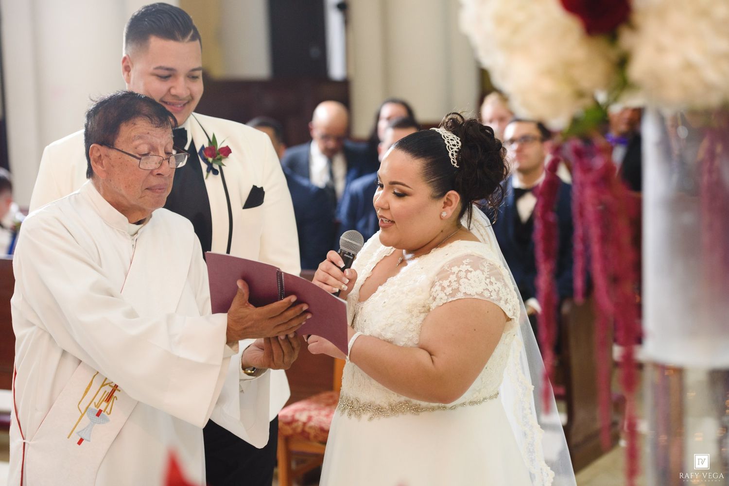 Bride reads wedding vows into microphone while officiant holds book during church wedding ceremony.