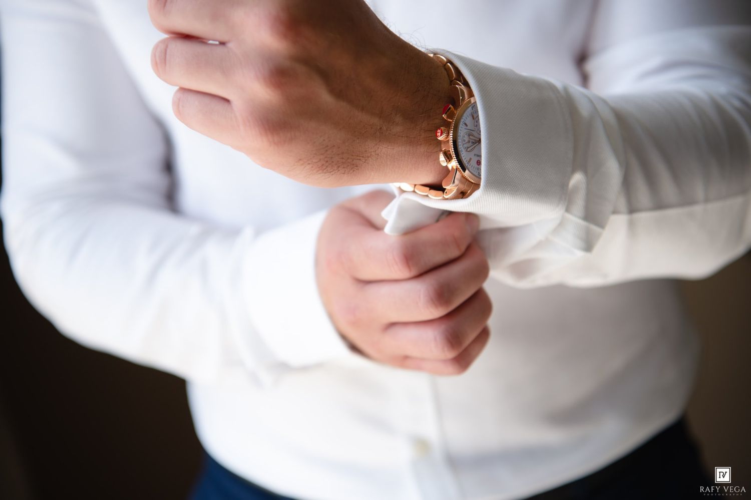 Man in white dress shirt fastening rose gold cufflinks, close-up detail shot for formal wedding attire.