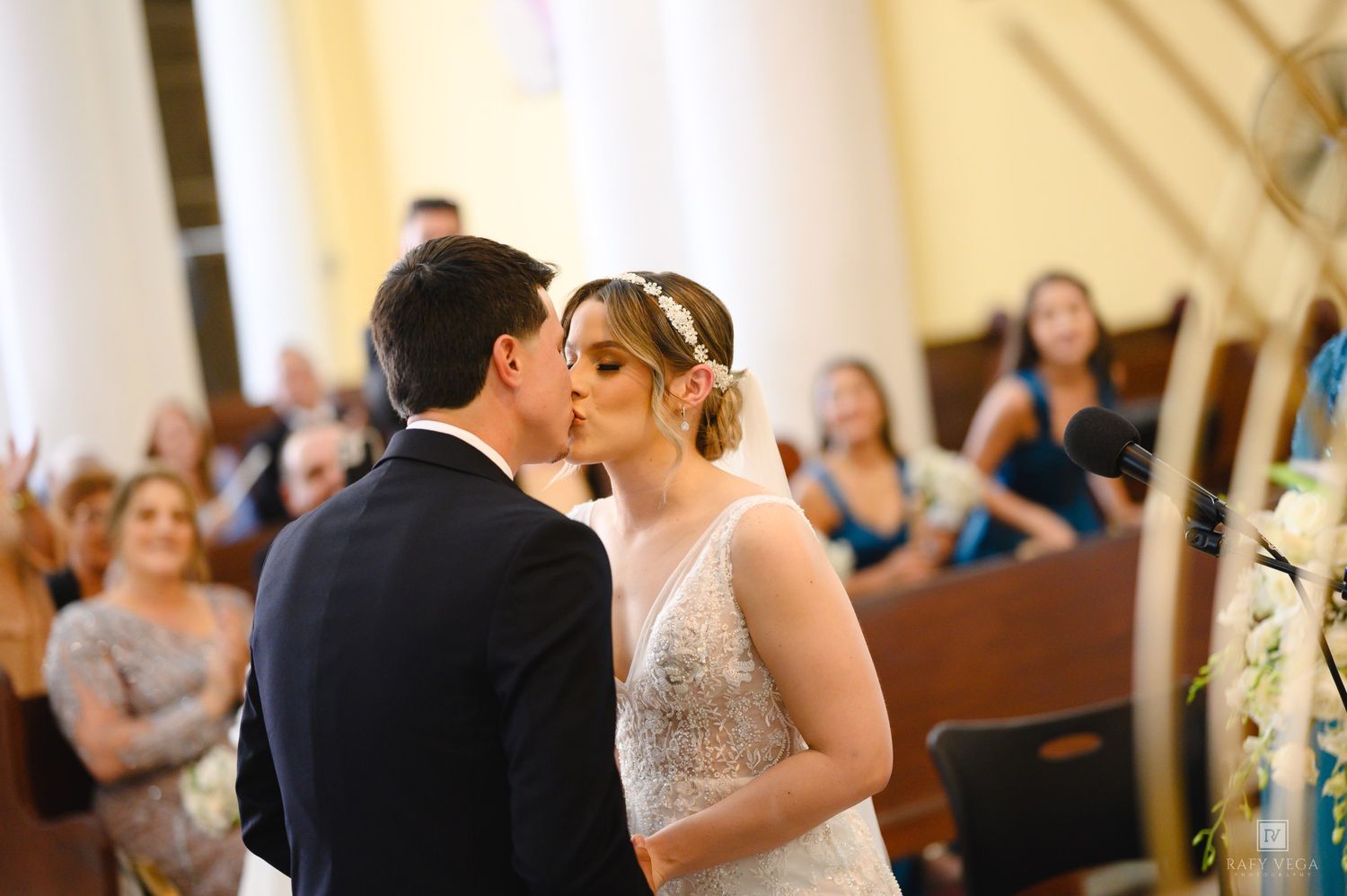 Bride and groom share their first kiss at the altar during a church wedding ceremony with guests watching.