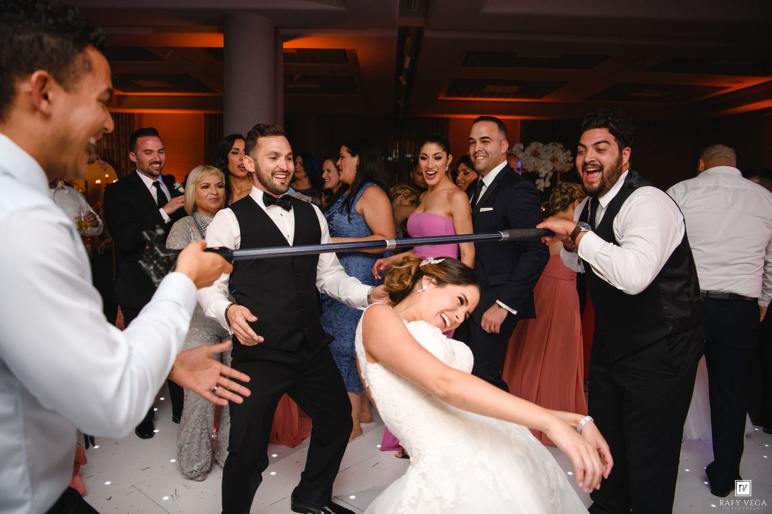 Bride and groom doing the limbo dance with wedding guests cheering at elegant reception venue.