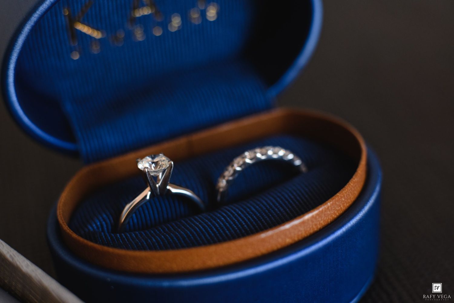 Close-up of a solitaire diamond engagement ring and eternity band in a luxury blue and gold ring box.