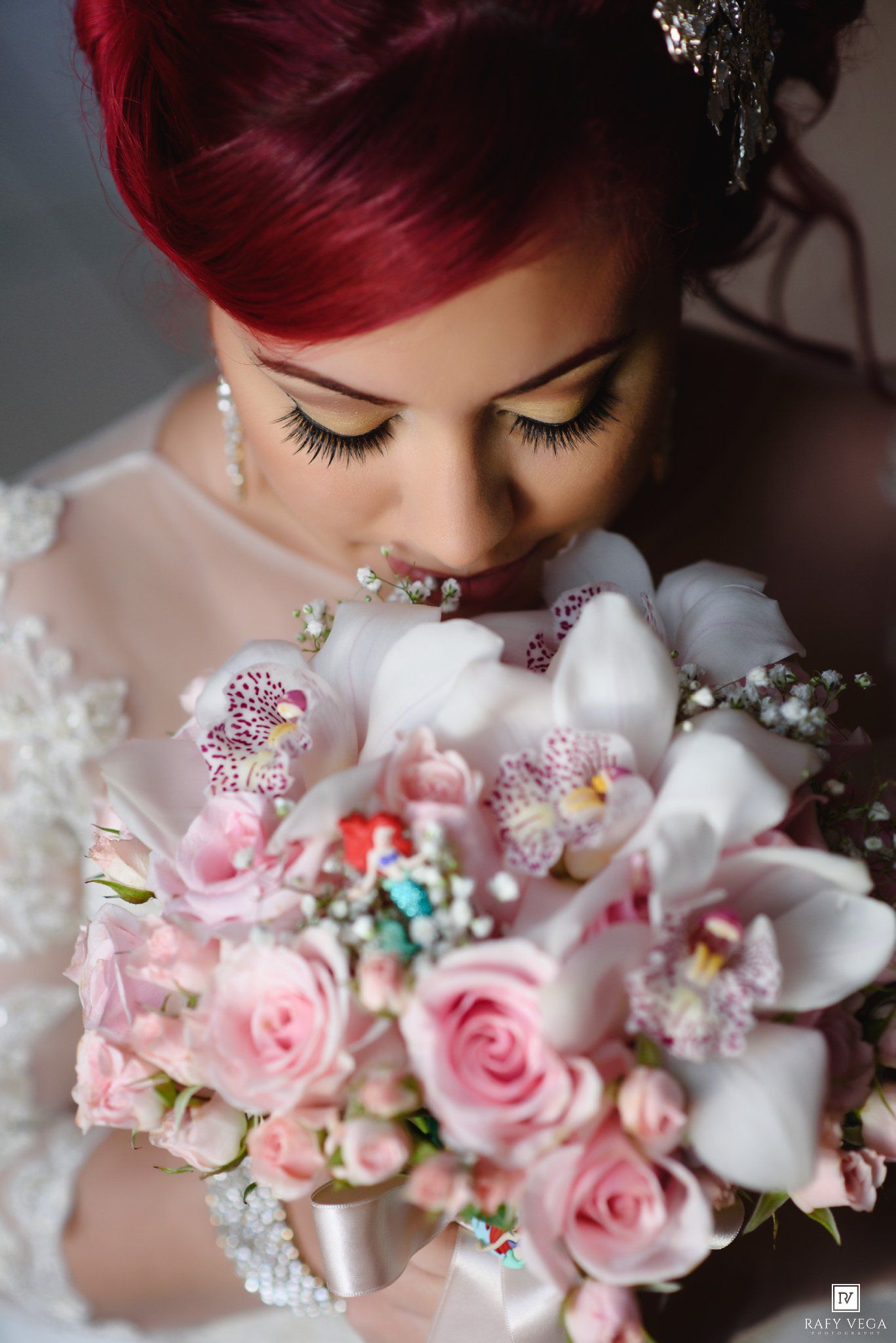 A bride with red hair smells her pink rose and white orchid wedding bouquet in a close-up portrait.