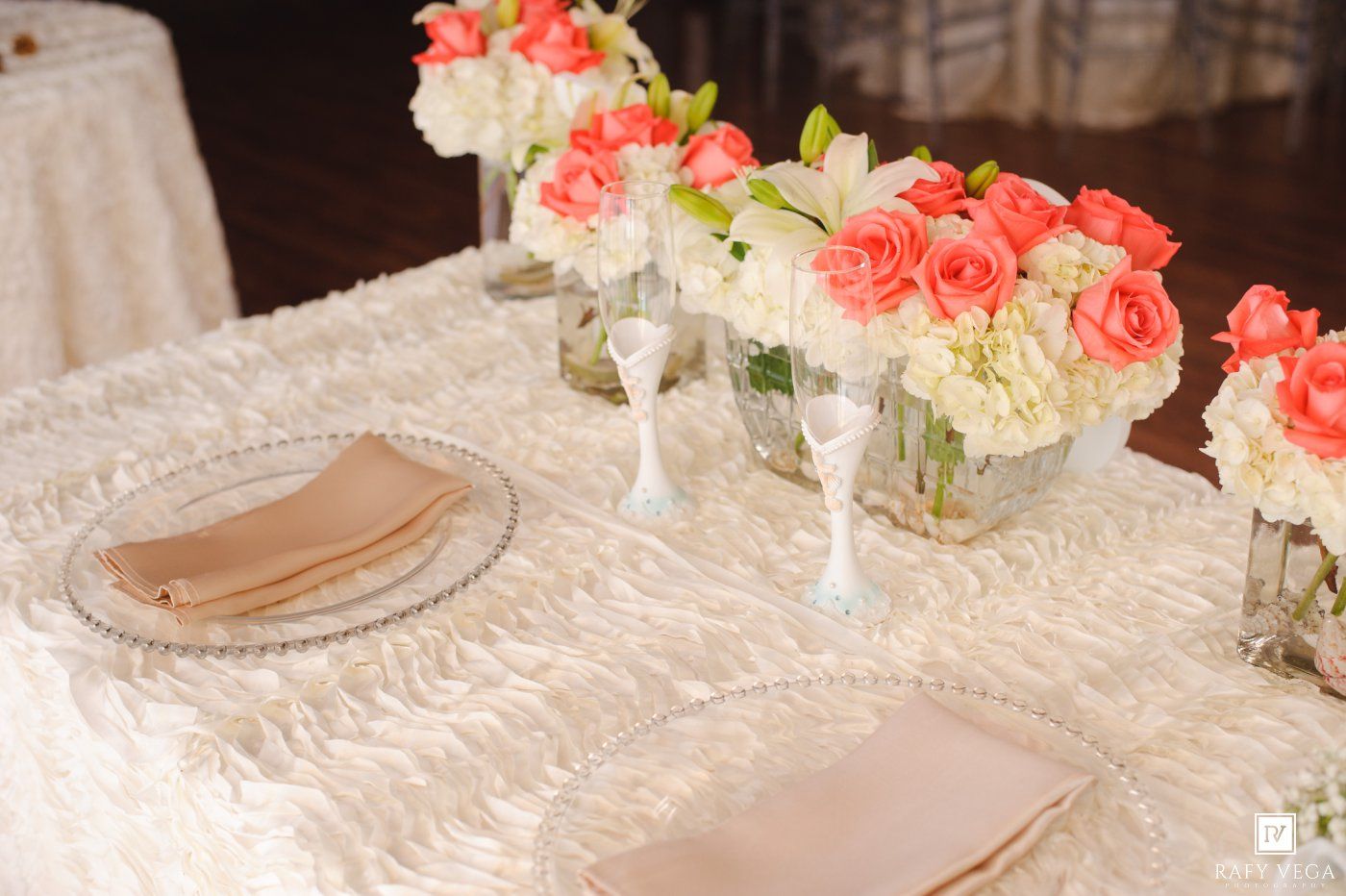Elegant wedding reception table with coral roses, white hydrangeas, and ivory ruffled linen centerpiece.