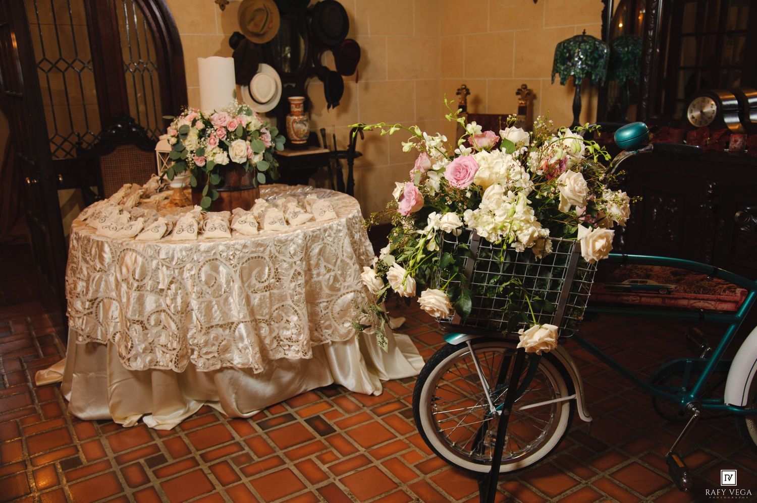 Elegant wedding reception table with gold rosette linen and floral arrangements beside a vintage bicycle with pink roses.