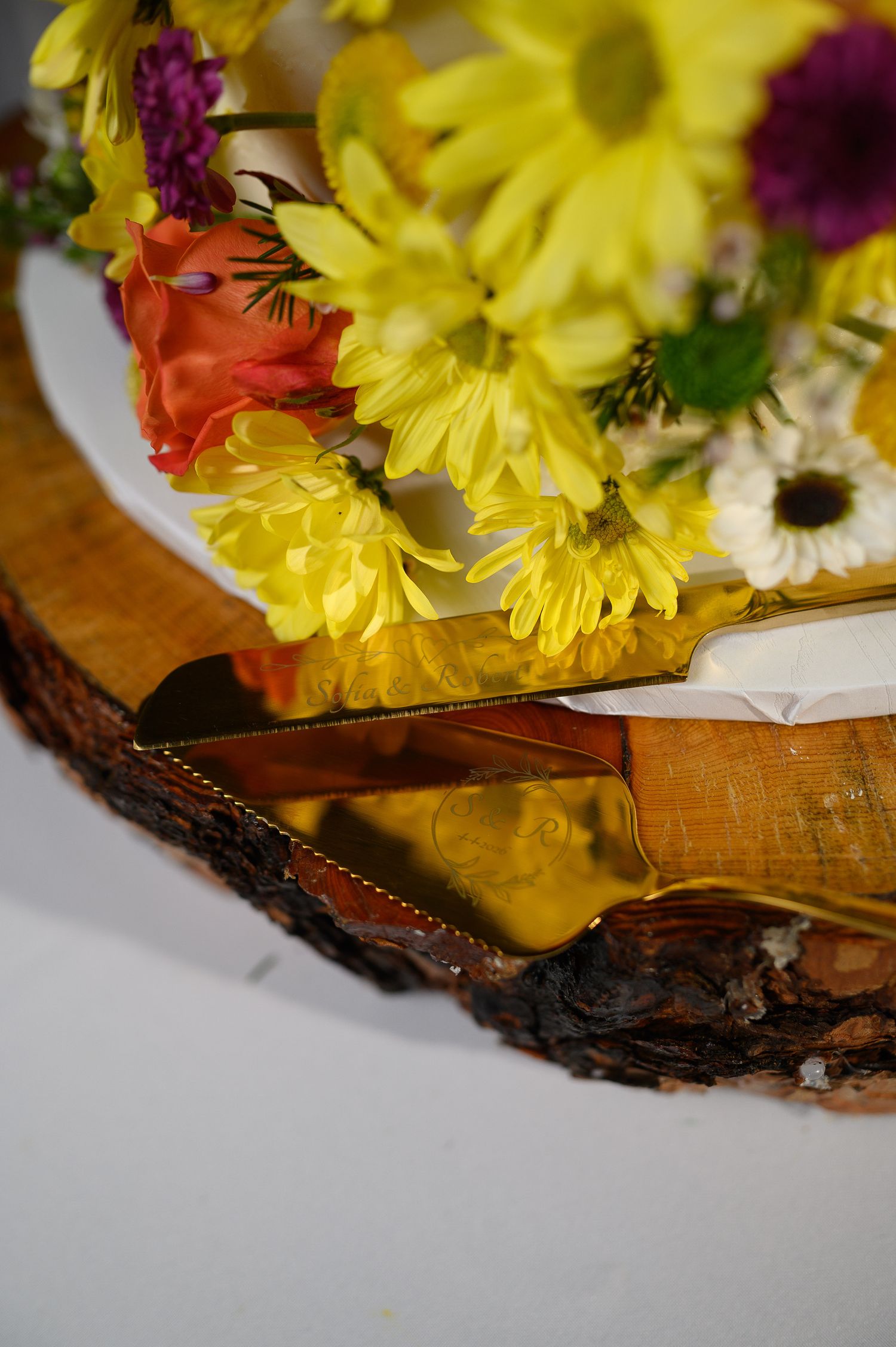 Rustic wood slice centerpiece with vibrant yellow daisies, orange roses, and mixed wildflowers on a white plate.