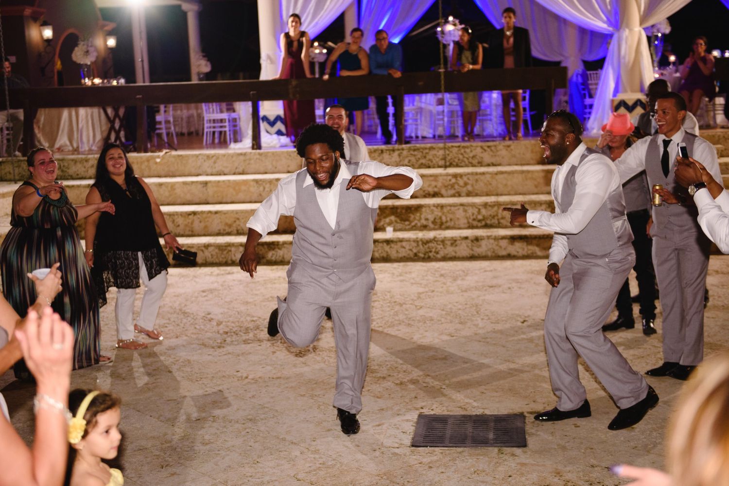 Men in gray suits dancing energetically at an outdoor wedding reception at night.