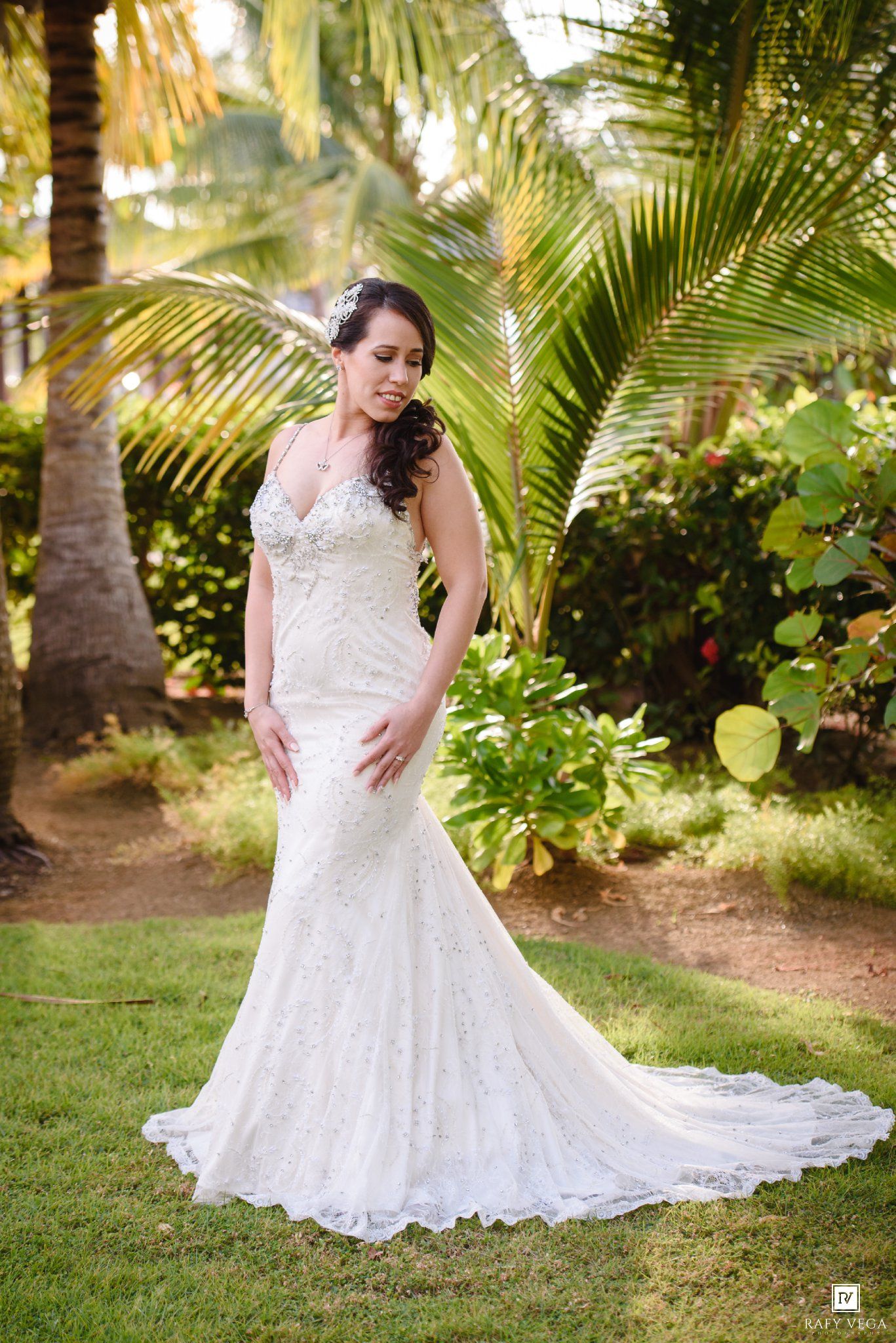 Bride in elegant lace mermaid wedding gown with beaded bodice posing in tropical garden with palm trees.