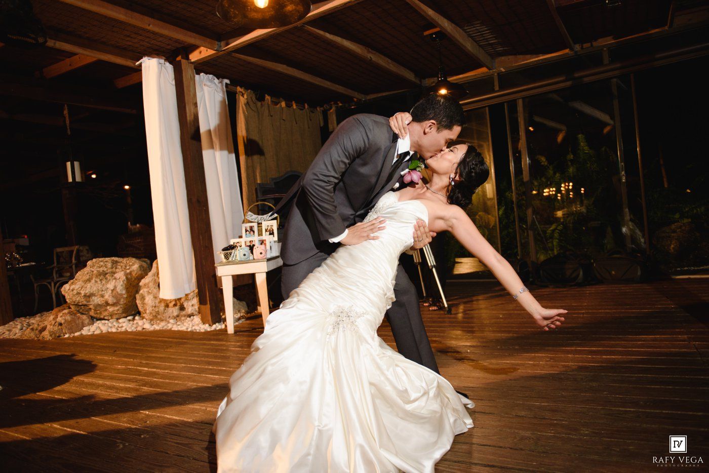 Groom dips bride for romantic first dance kiss at outdoor wedding reception.