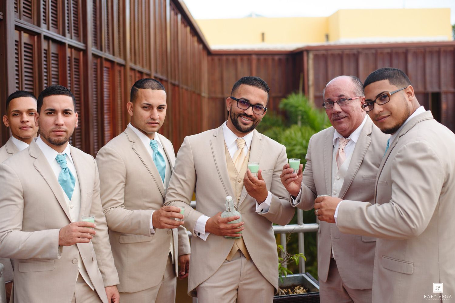 Groom and groomsmen in matching tan suits with blue and gold ties posing outdoors.