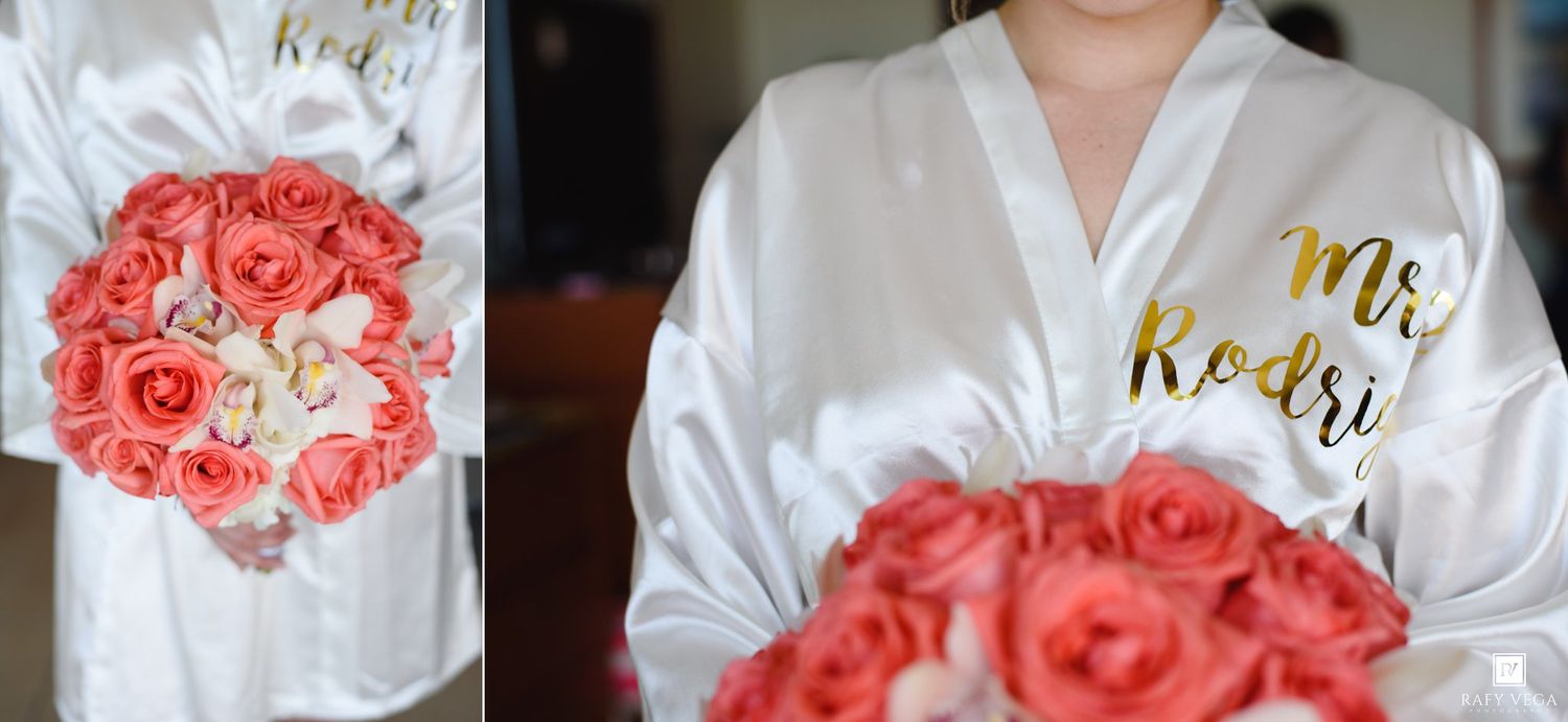 Bride in white satin Mr. Rodri robe holding a vibrant coral rose bouquet on her wedding day.