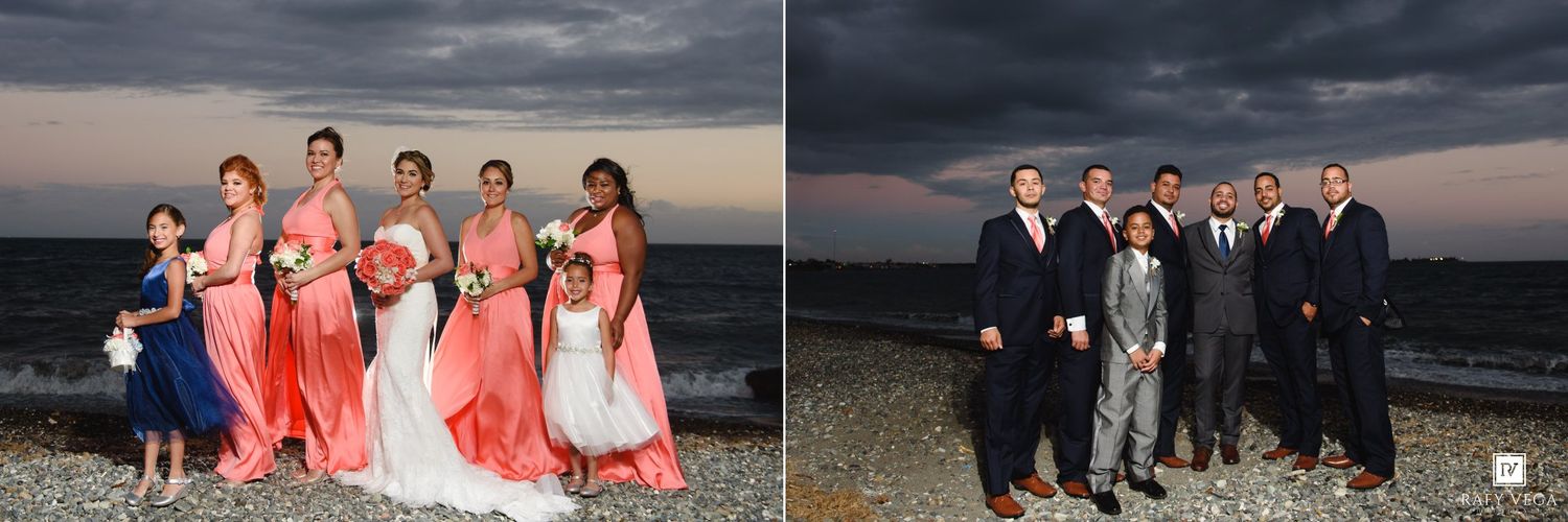 Wedding party poses on rocky beach under dramatic stormy sky, bridesmaids in coral gowns and groomsmen in navy suits.