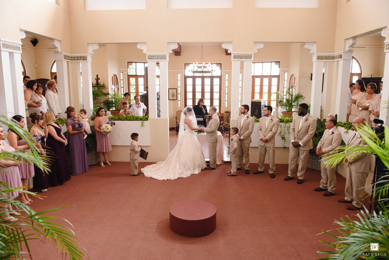 Wide angle view of wedding ceremony with bride, groom, and full wedding party at altar.