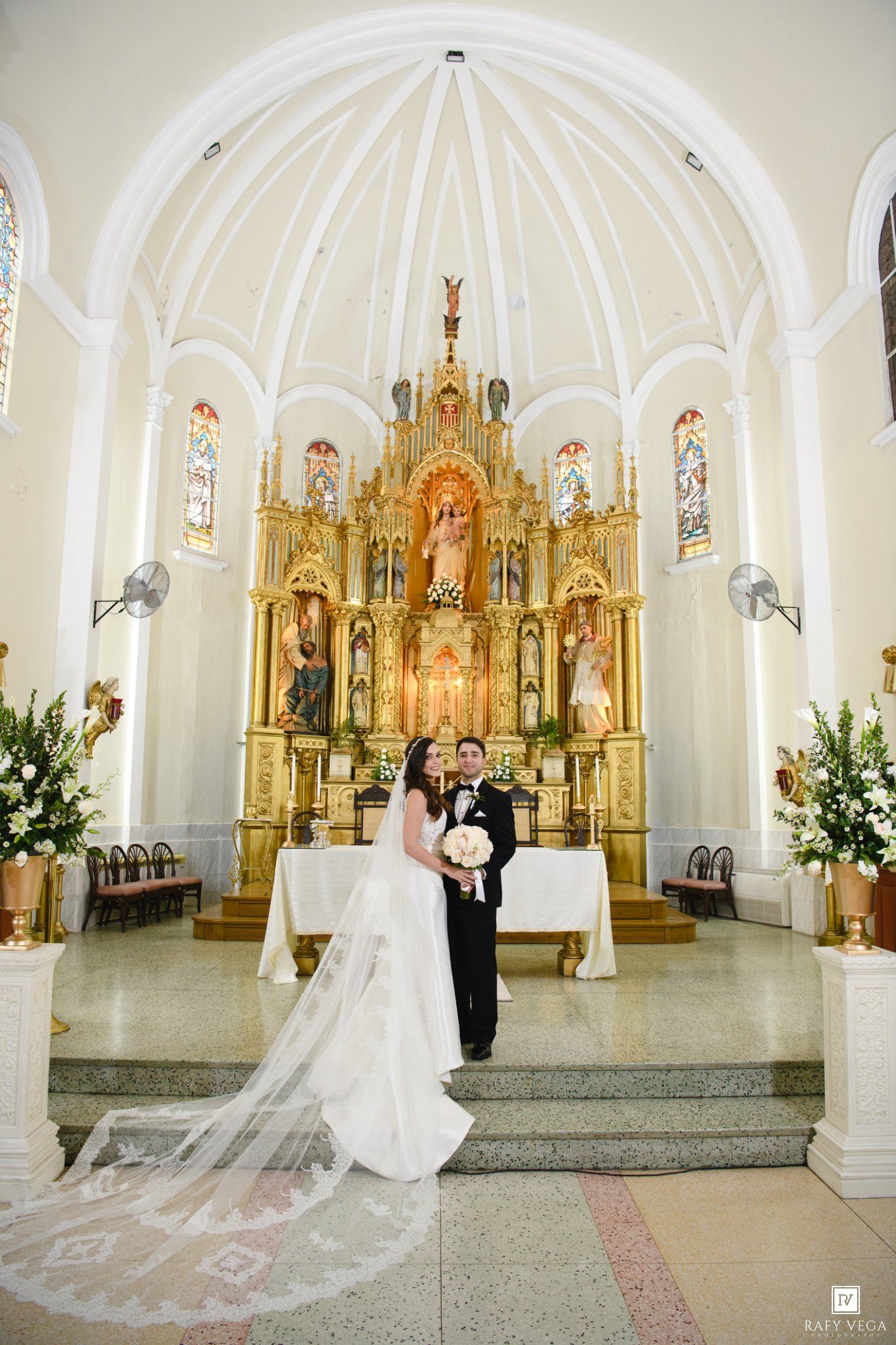 Newlyweds pose before ornate golden altar in elegant church with arched ceiling.