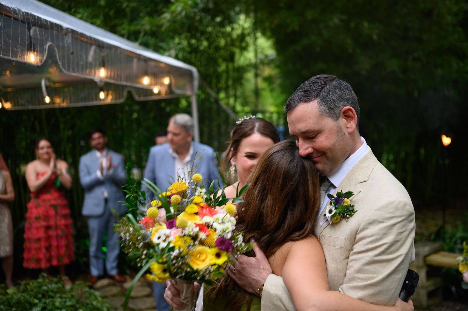 Bride and groom share a heartfelt embrace during outdoor wedding ceremony with colorful bouquet.