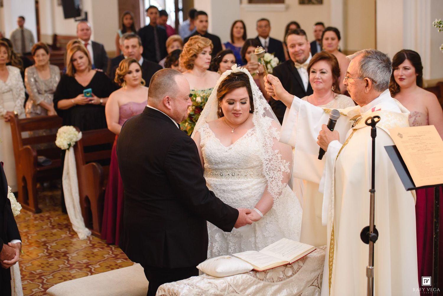 Bride and groom exchange vows at church altar during wedding ceremony with guests and bridesmaids in background.