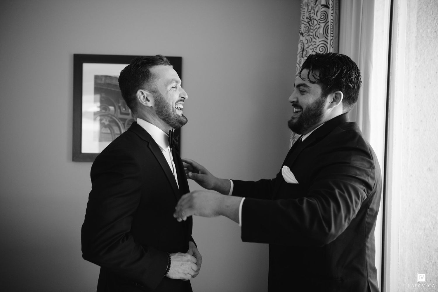 Groomsmen helping groom adjust his tie in black and white wedding preparation photo.