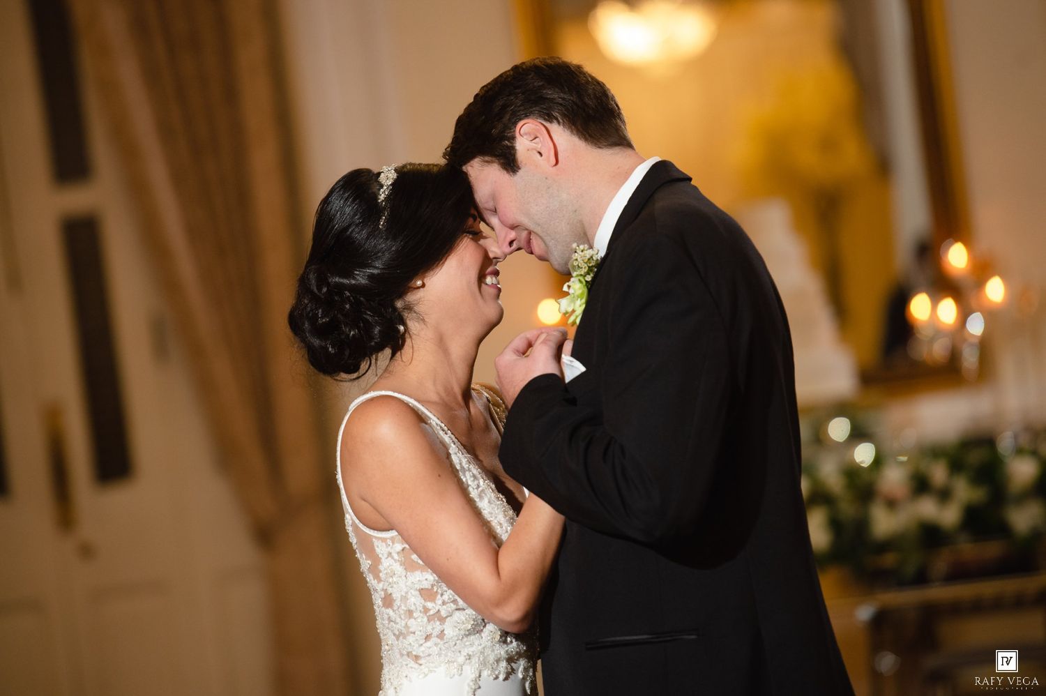 Bride and groom share a romantic first kiss at elegant wedding reception with candlelit background.