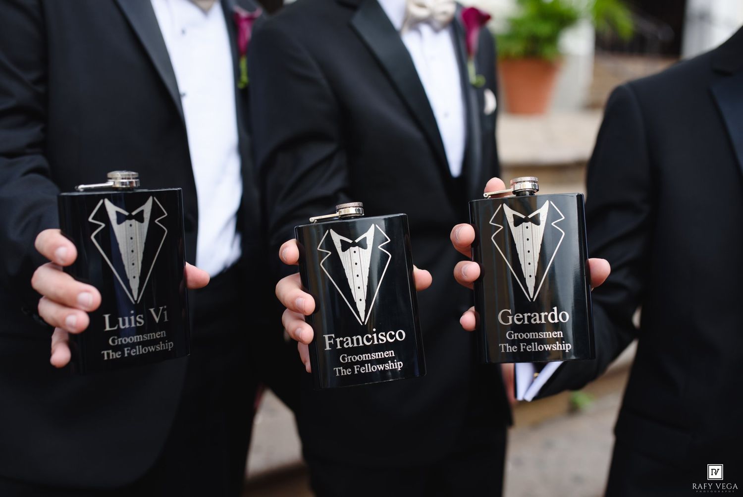 Groomsmen holding personalized black tuxedo flasks engraved with names Luis, Francisco, and Gerardo for The Fellowship wedding.