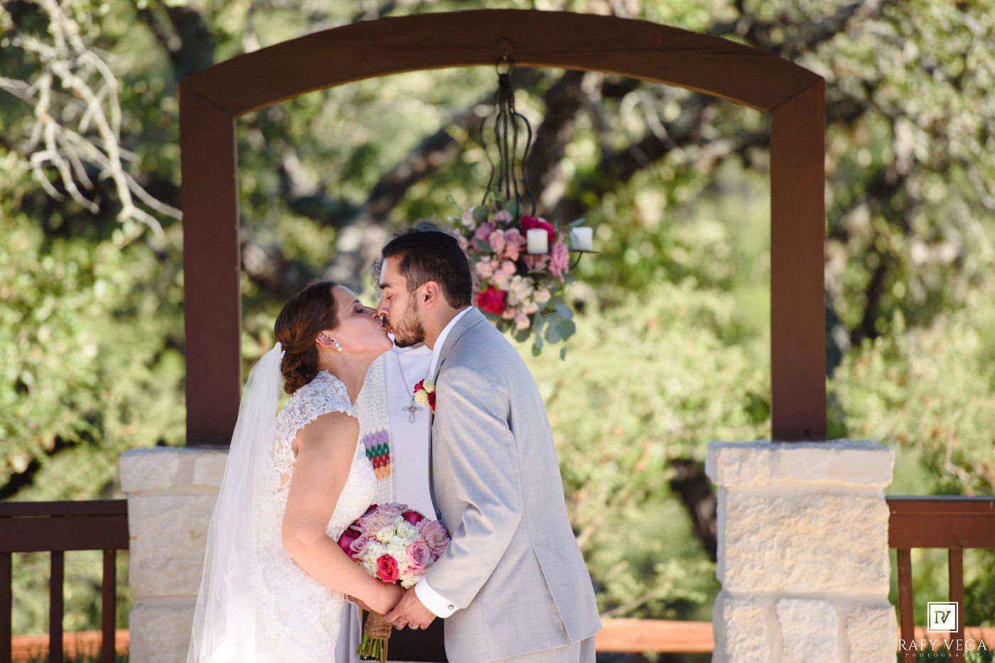 Bride and groom share their first kiss under a floral arch at an outdoor wedding ceremony.