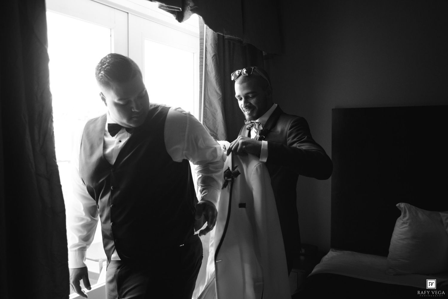 Groom getting dressed with groomsman assistance in black and white wedding preparation photo.