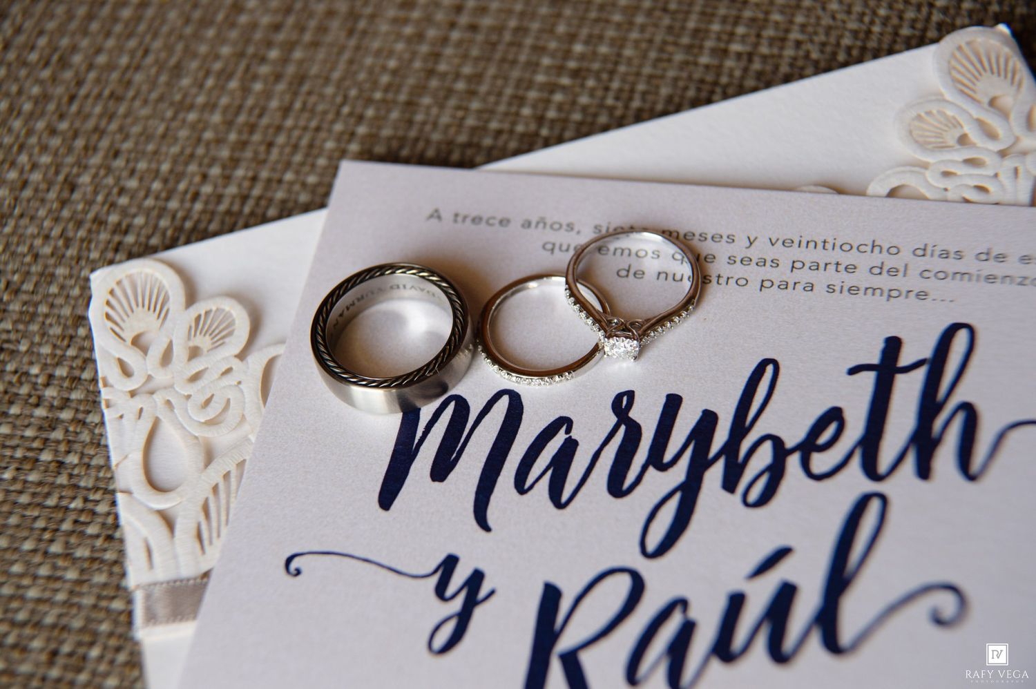 Two gold wedding bands resting on an elegant laser-cut wedding invitation for Marybeth and Raul.