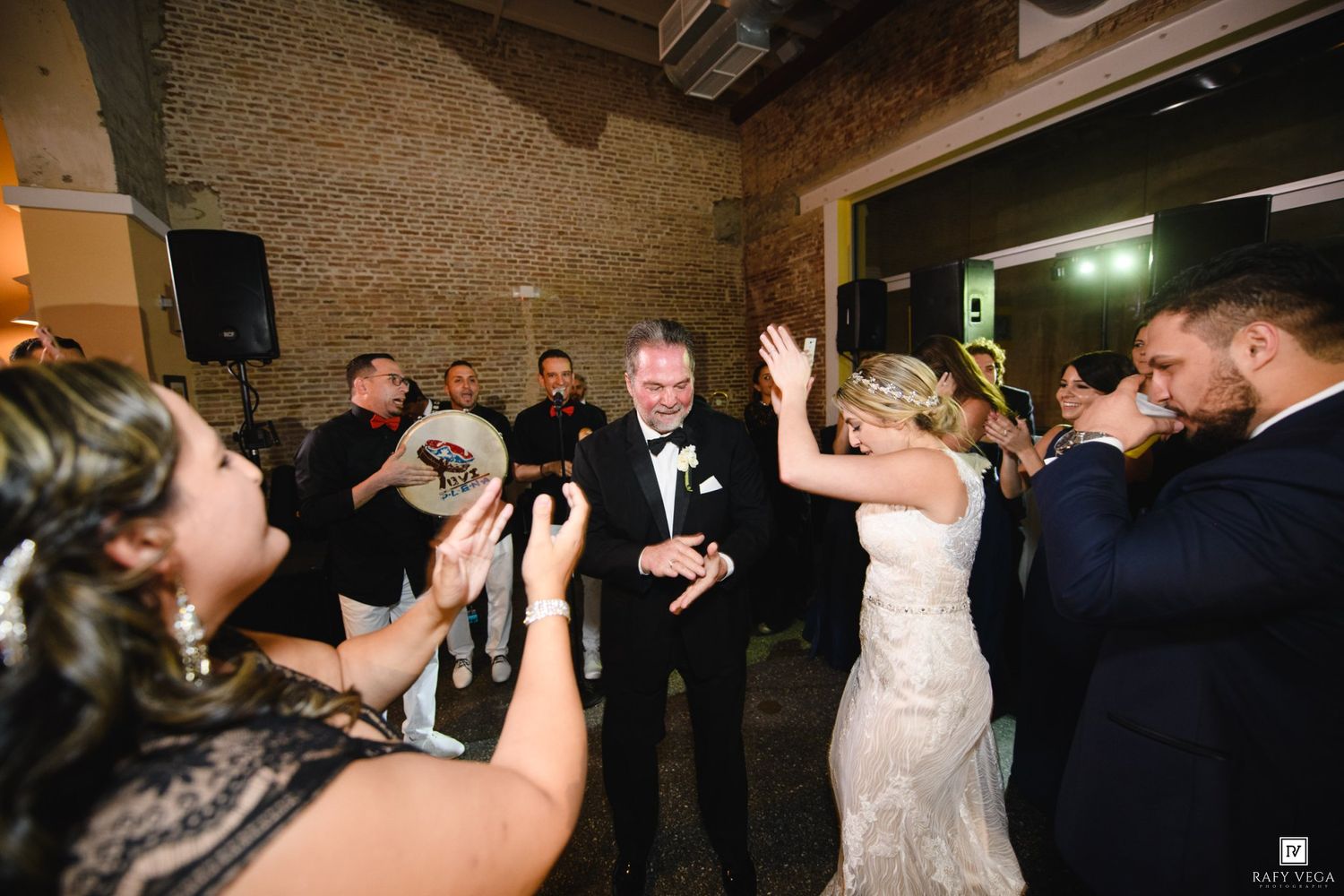 Bride and groom celebrate with guests on the dance floor at a festive indoor wedding reception.