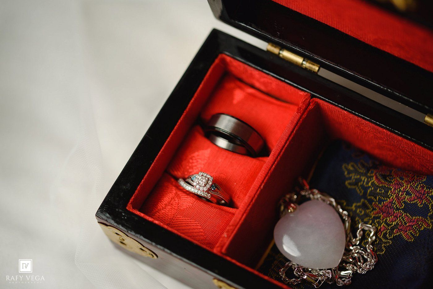Wedding rings displayed in a red velvet Chinese jewelry box with decorative jade ornament beside it.