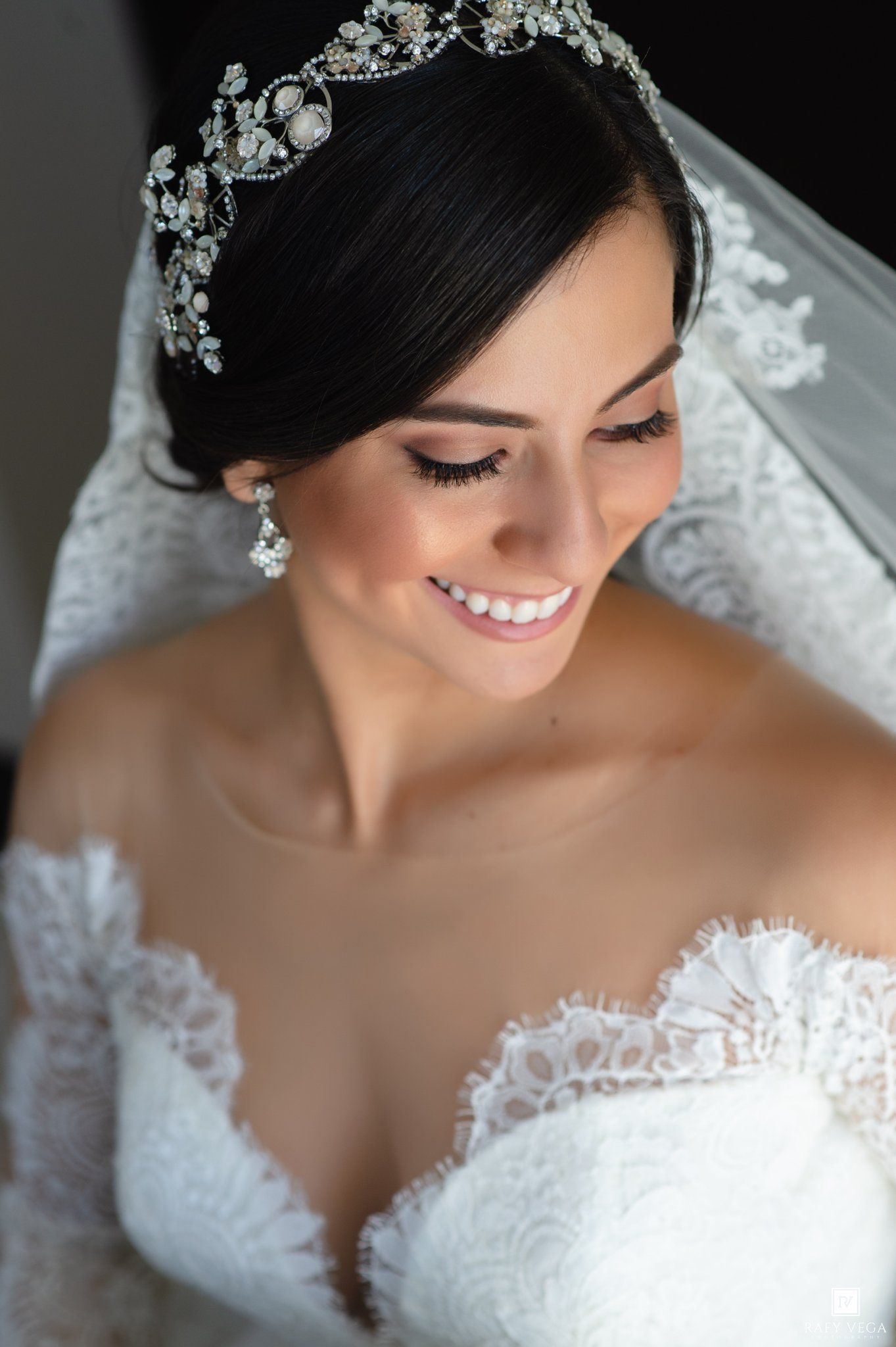 Smiling bride wearing a crystal tiara, lace wedding gown, and floral earrings on her wedding day.