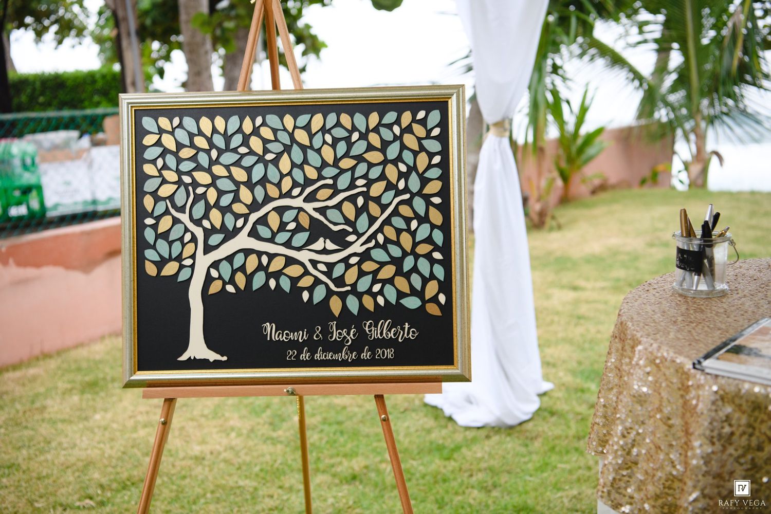 Wedding guest book sign featuring a decorative tree with colorful leaves on an easel, personalized with the couple's names and date.