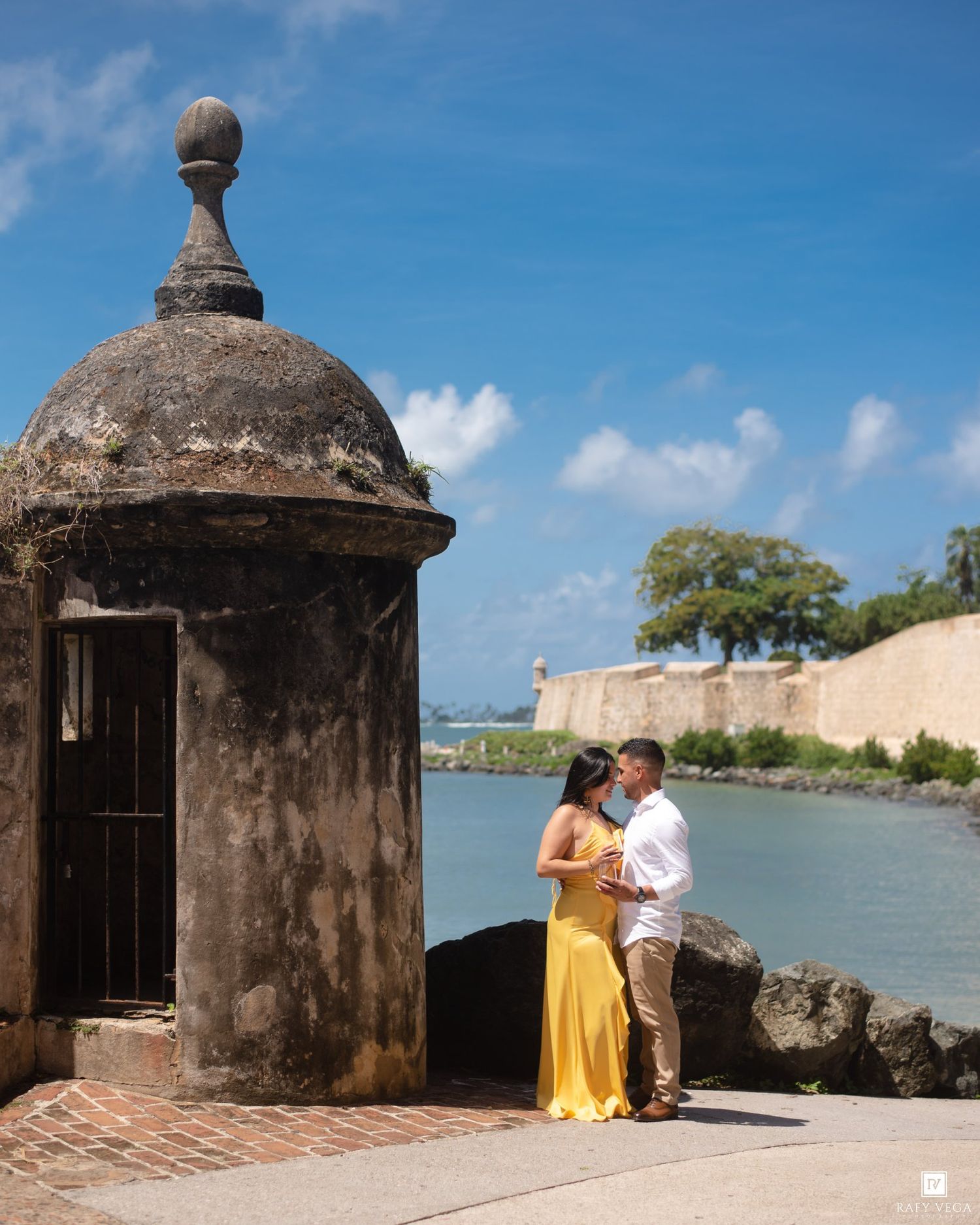 Couple kissing in yellow dress near historic stone sentry box at Castillo San Felipe del Morro, Old San Juan, Puerto Rico.